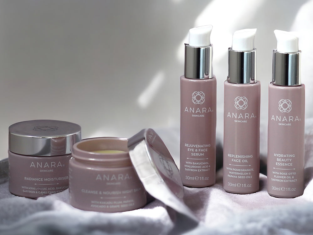 Radiance Moisturiser, Cleanse & Nourish Night Balm with the lid open, Rejuvenating Eye & Face Serum, Replenishing Face Oil, Hydrating Beauty Essence. All placed on a light grey soft and cosy blanket