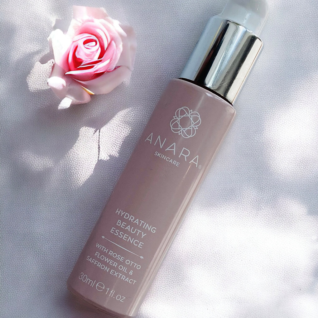 Anara Hydrating Beauty Essence bottle in the sunshine with a pink rose.