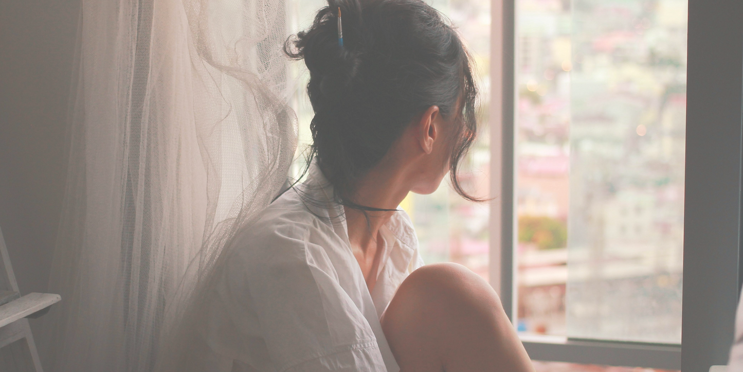 Lady with dark brown hair and a white shirt looking out of the window