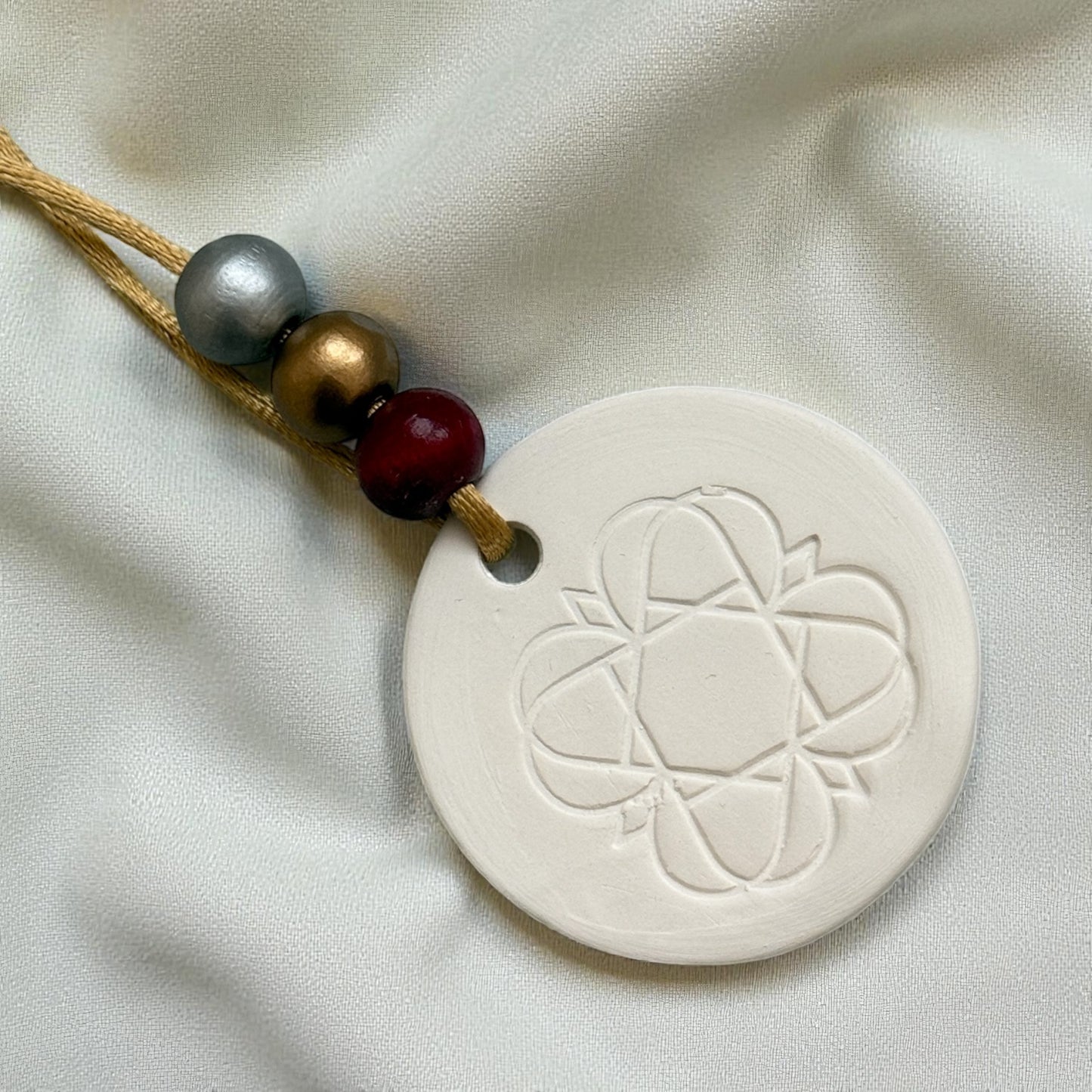 
                  
                    Anara emblem keepsake scent diffuser with beaded hanging on cream fabric
                  
                