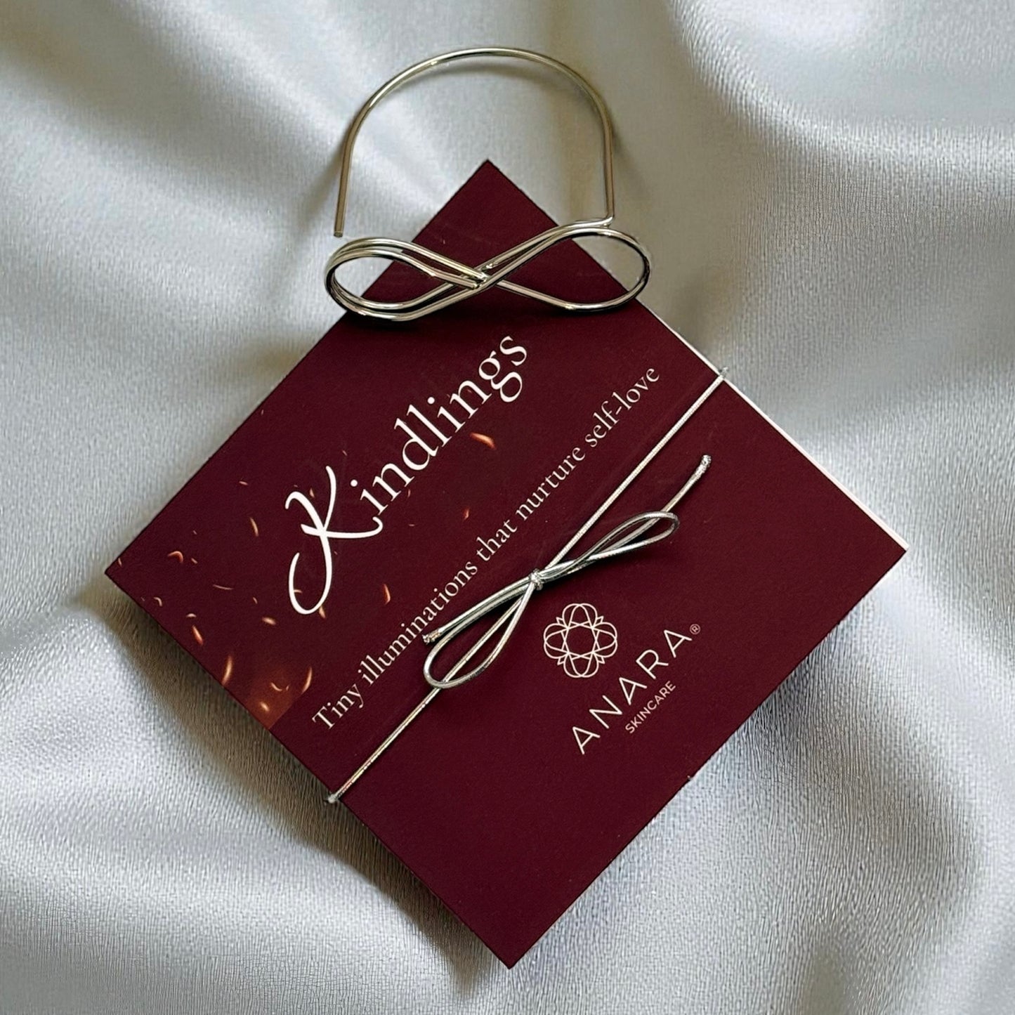 
                  
                    Anara Kindlings set and metal infinity holder on silver fabric
                  
                