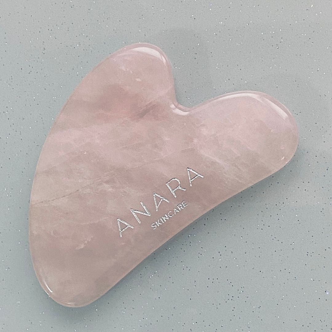 
                  
                    Pink gua sha tool with 'ANARA SKINCARE' branding on a grey background
                  
                