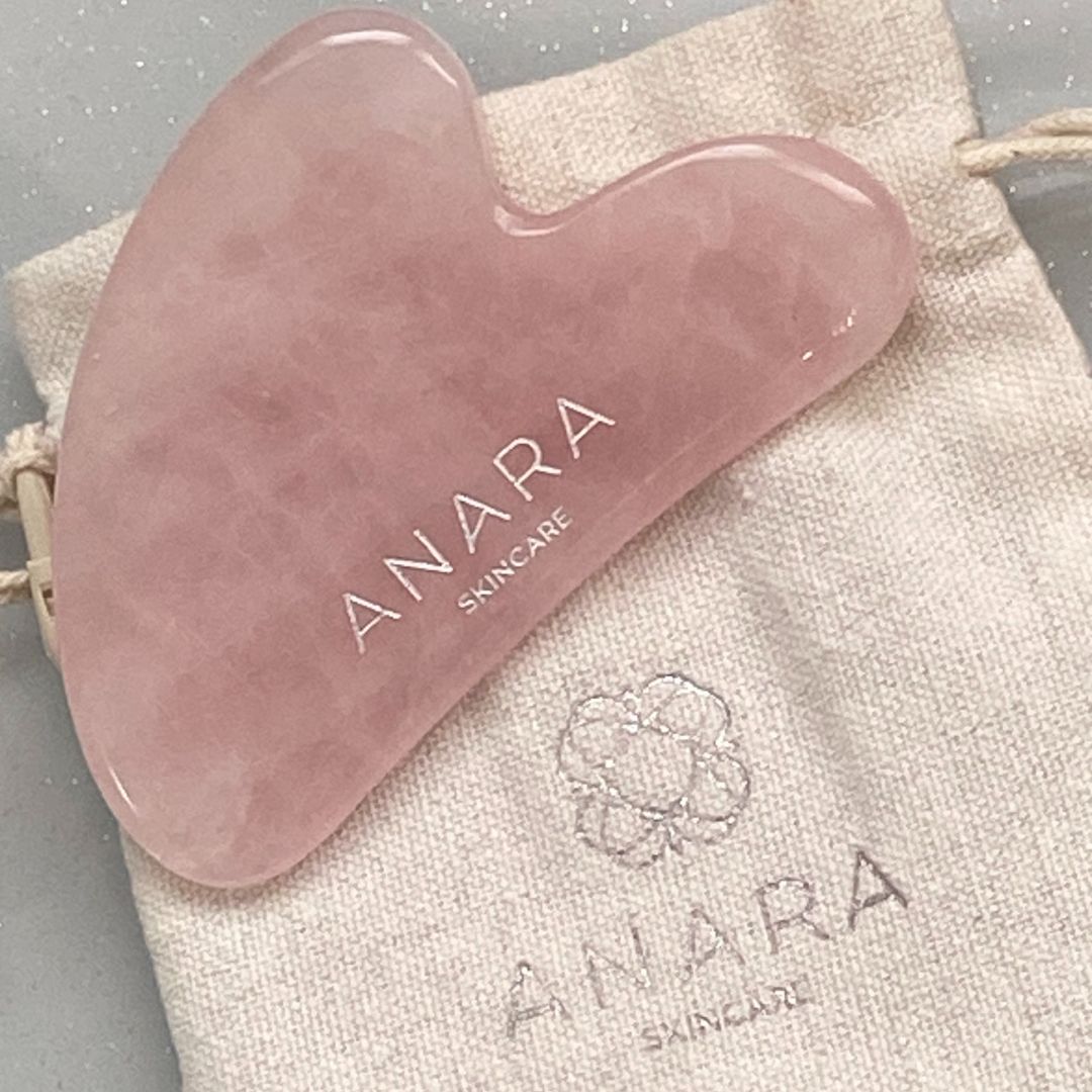 
                  
                    Pink gua sha tool with 'ANARA SKINCARE' branding on a matching fabric pouch.
                  
                