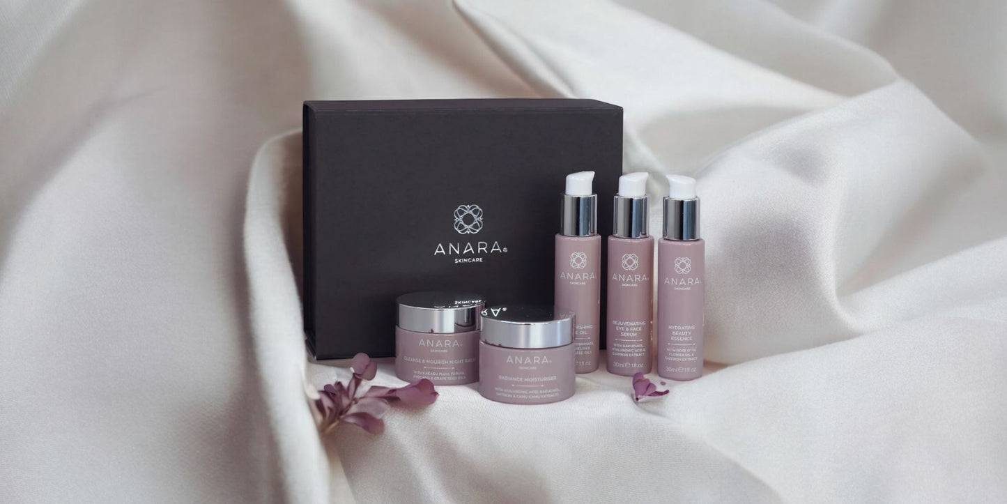 Anara skincare products including bottles and jars on a cream fabric with a grey gift box in the background.