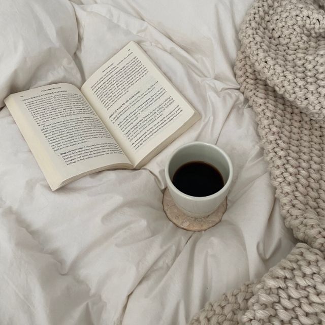 Open book and cup of coffee on a soft surface with a knitted blanket.