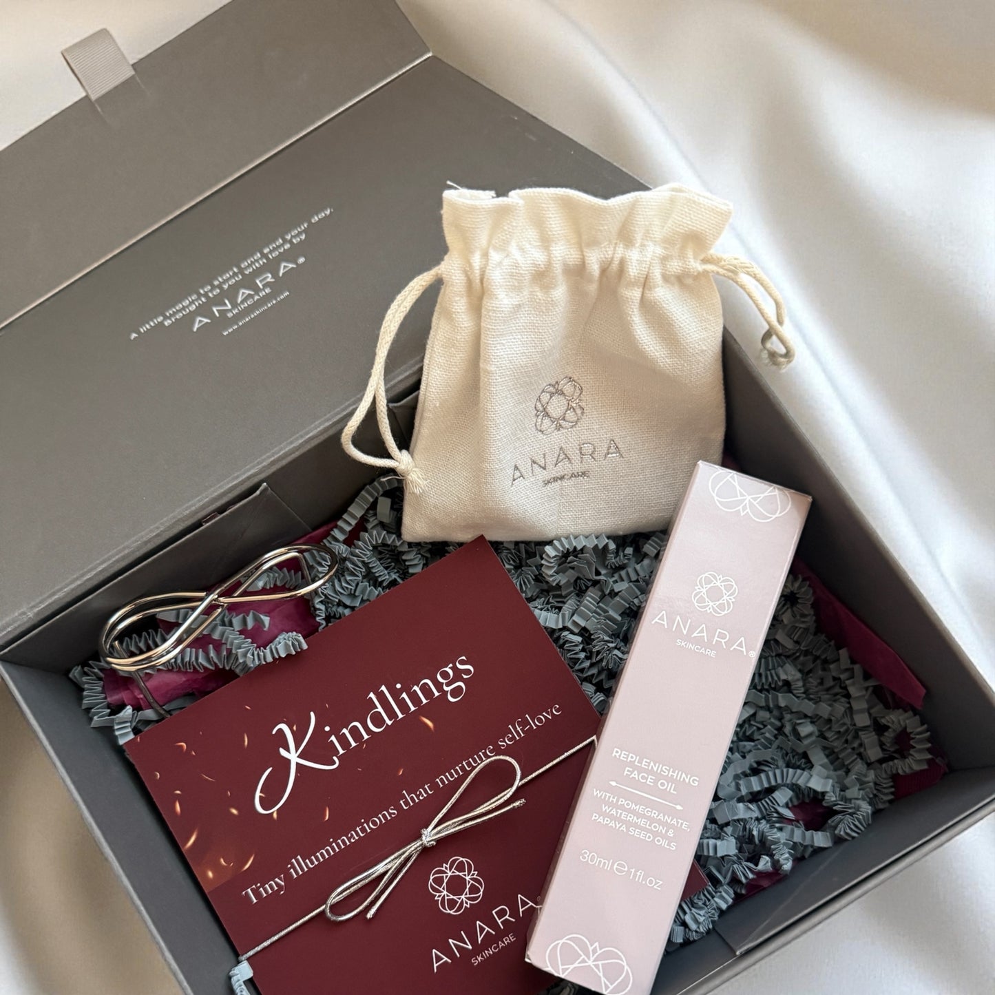 Anara Kindlings, metal infinity holder, Rose quartz Gua Sha pouch and Replenishing Face Oil in carton in gift box