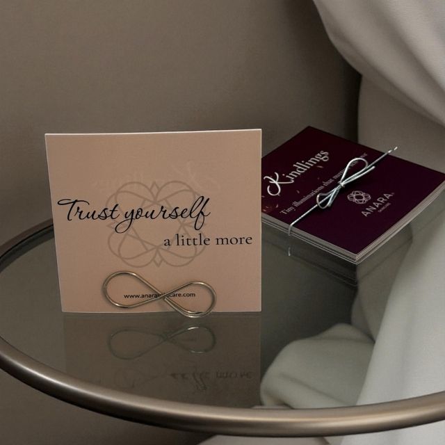 Anara Skincare Kindlings Card with 'Trust yourself a little more' message and infinity symbol on a glass table with the full set of Kindlings in the background