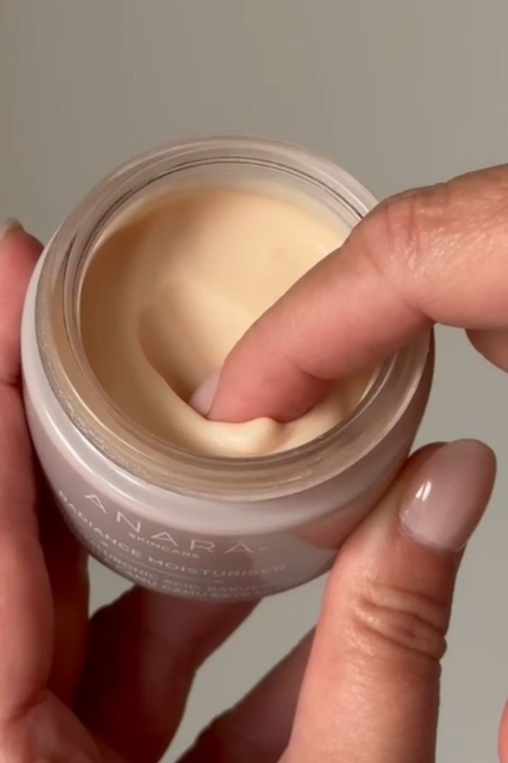 Woman holding a jar of Anara Radiance Moisturiser, scooping with her finger