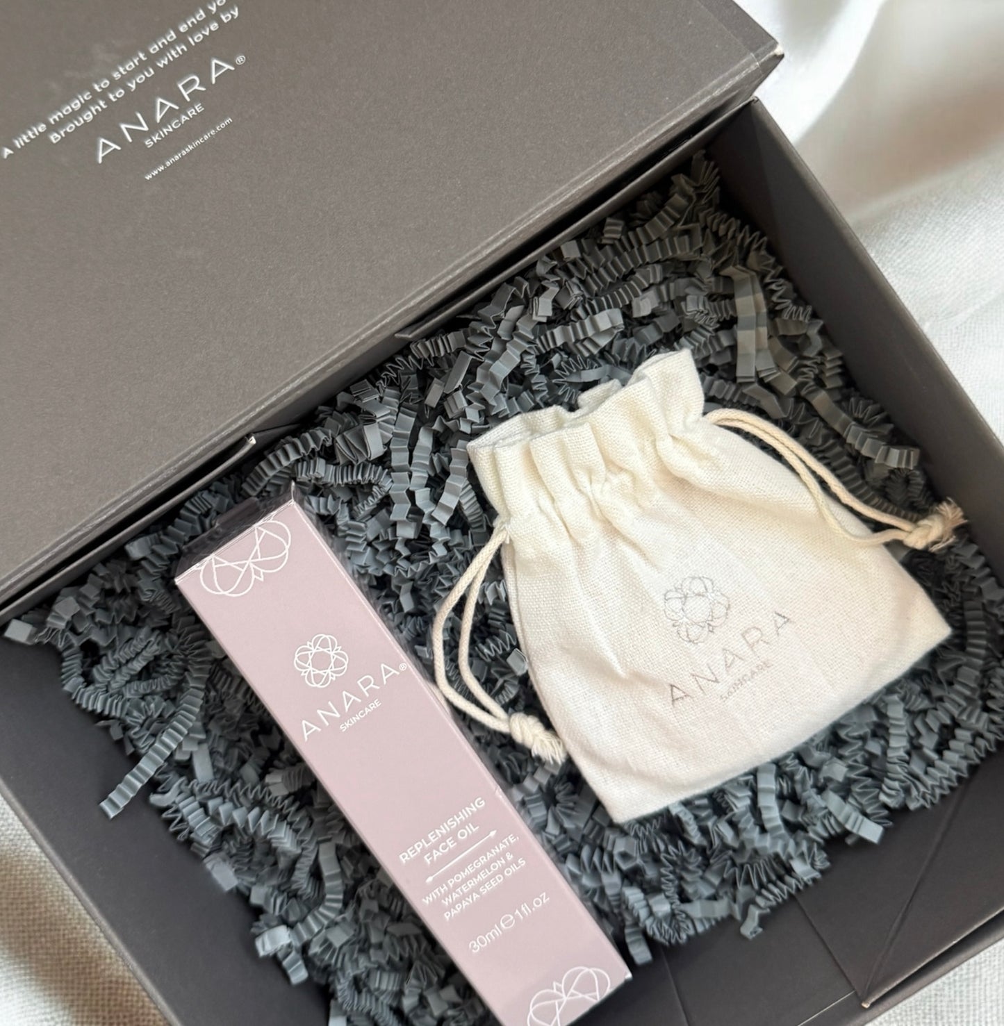 Anara Replenishing Face Oil and Rose Quartz Gua Sha in their outer cartons presented in grey Anara branded magnetic gift box