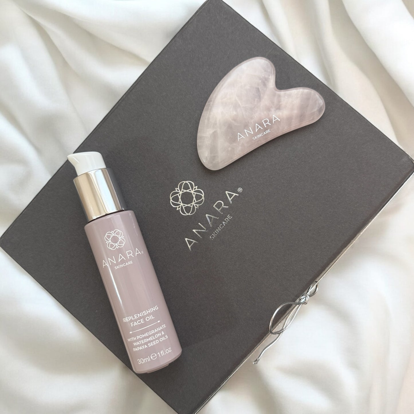 Anara Replenishing Face Oil with Rose Quartz Gua Sha on grey magnetic gift box with Anara logo in silver
